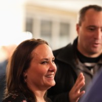 Woman smiling at other person and man behind her is talking with his hands